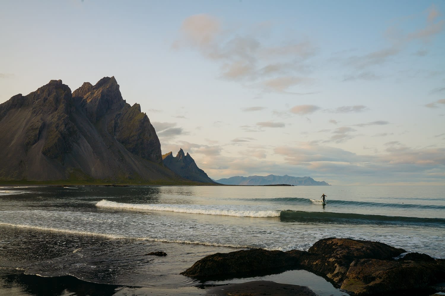 Vestrahorn in East Iceland pictured on a calm, blue sky, day where a person can be seen wading through the water towards the camera