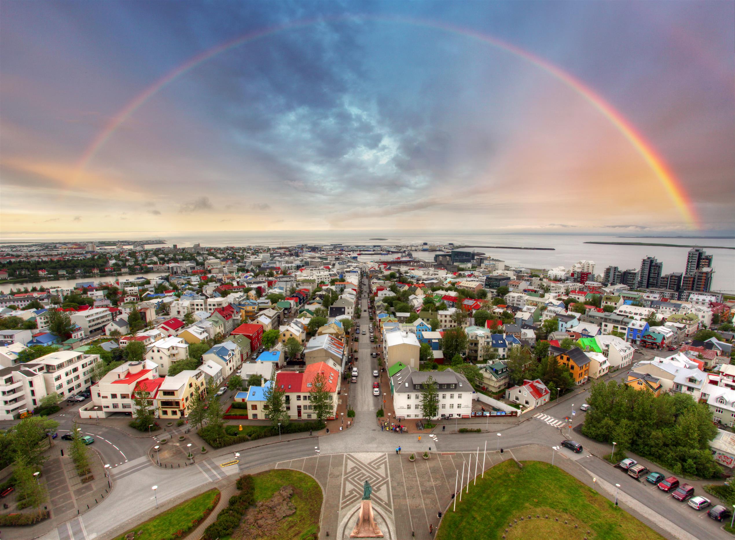 An overhead view of Reykjavik city on a bright day with a rainbow overhead that circles across the city