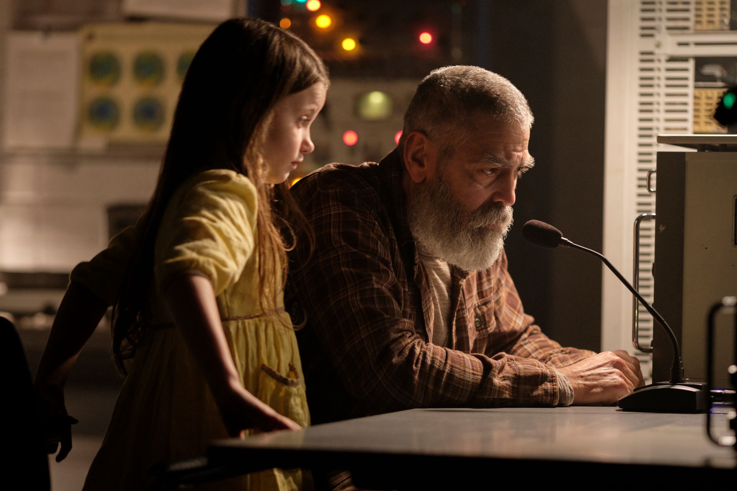 George Clooney pictured with a young girl during the filming of The Midnight Sky. Both are pictured looking at a computer screen