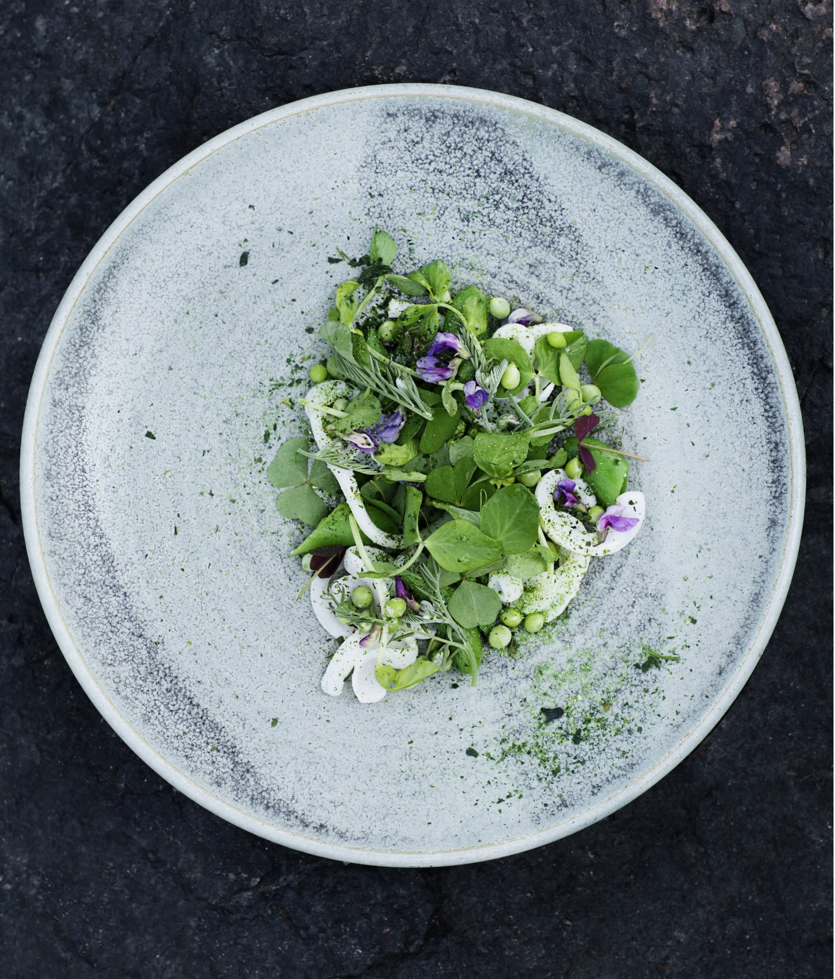 an overhead picture of a grey plate with a leafy vegetable salad dish upon it