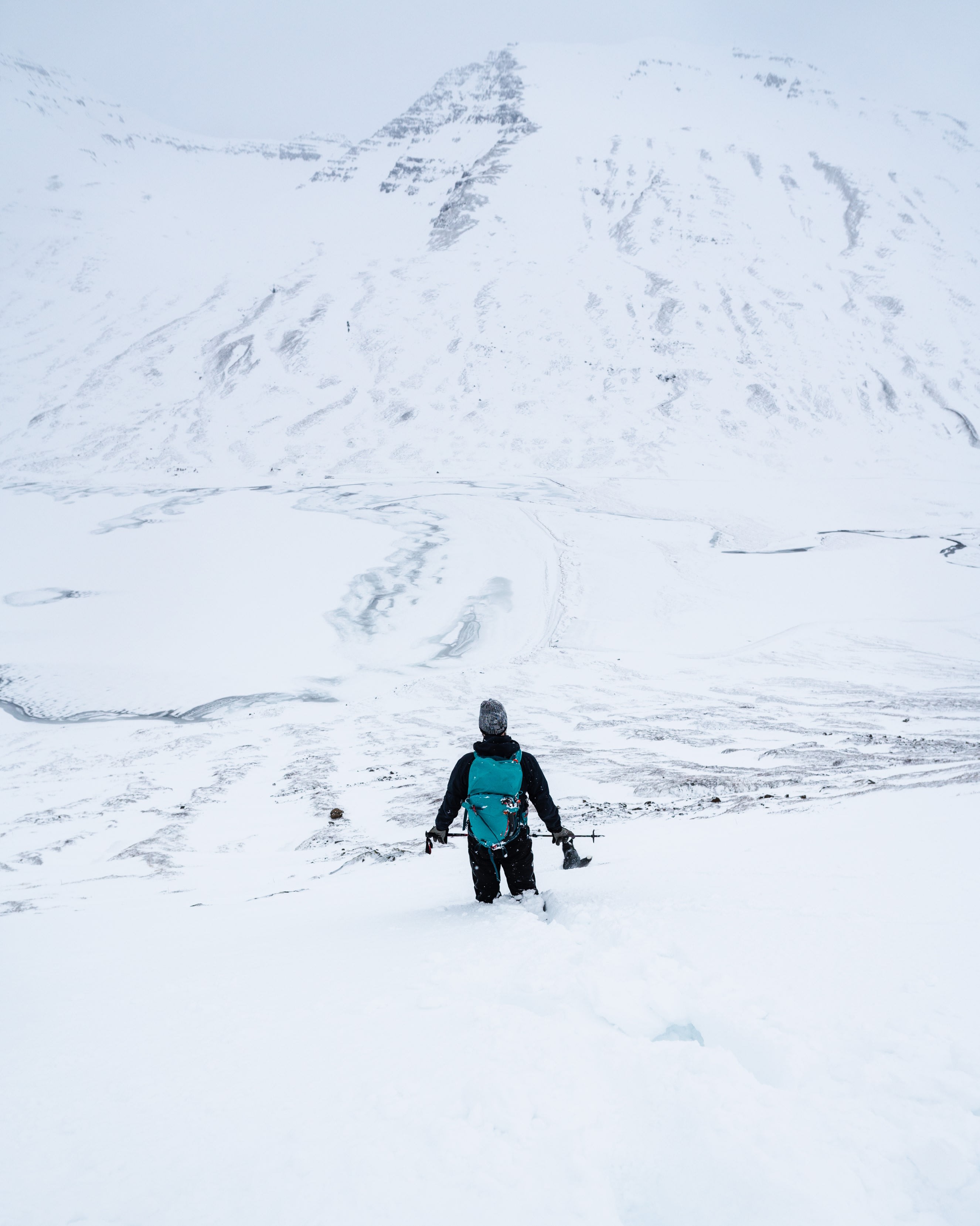 a person wearing all black with a blue backpack standing in a snowy Icelandic mountain region