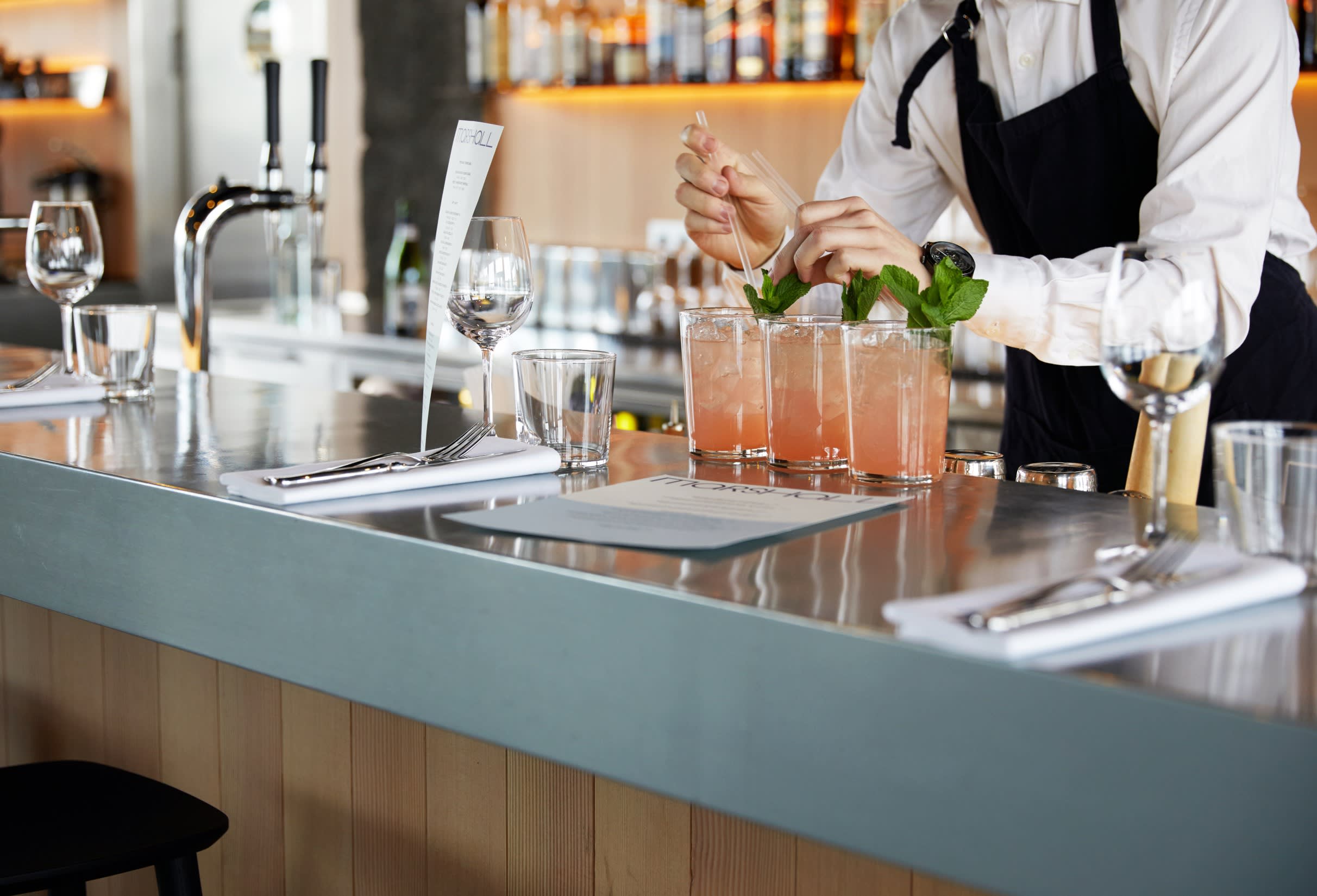 a bartender prepares three cocktails at the bar in Marshall's