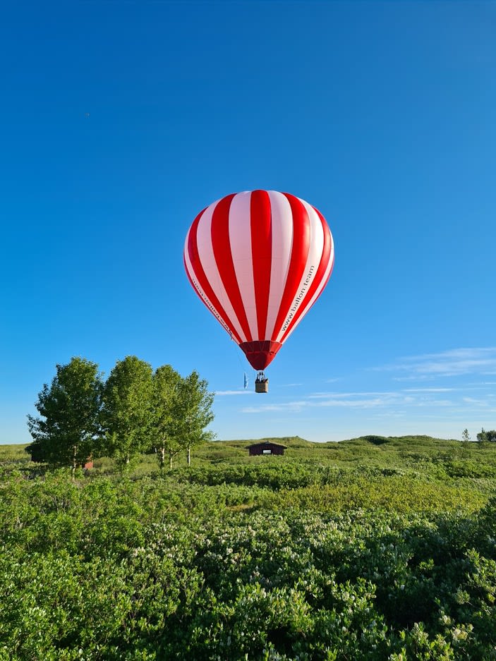 a red and white striped hot air balloon floating above a lush green landscape in Iceland