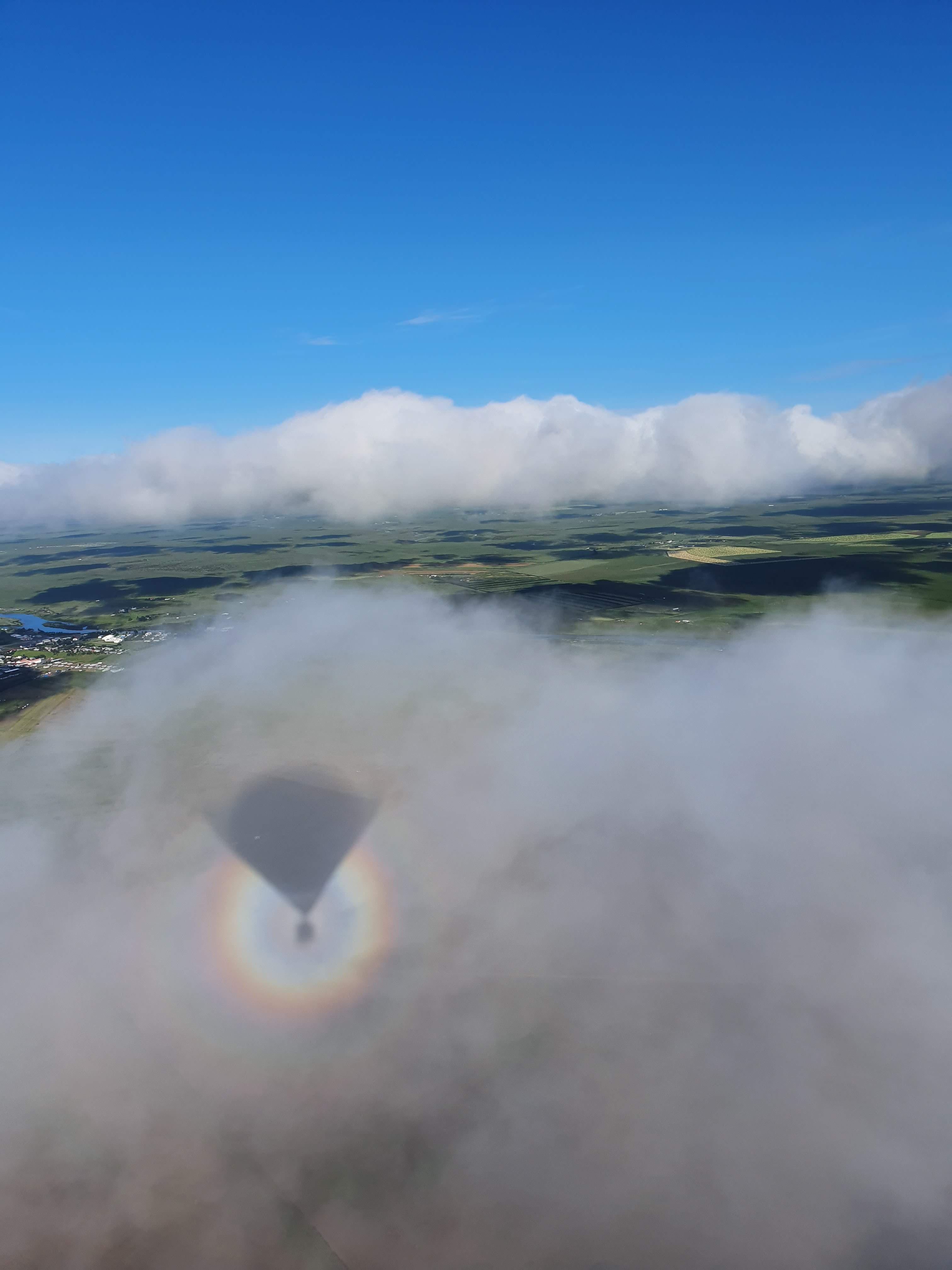 a view from within the hot air balloon looking out over the clouds and fertile land beneath