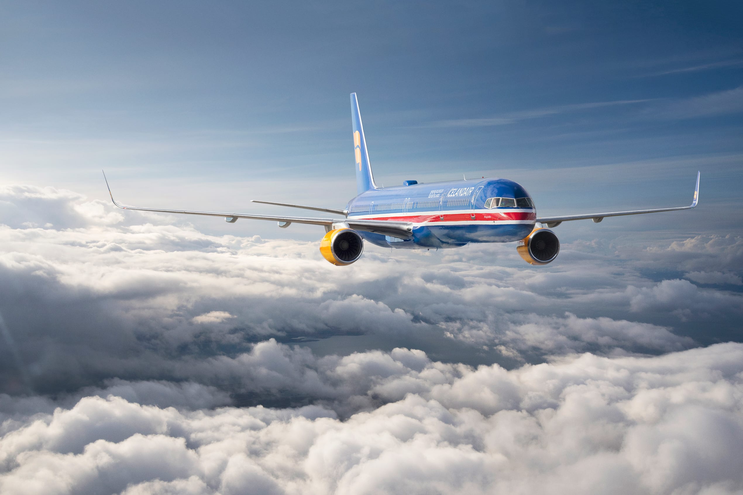 a blue Icelandair airplane flies over the clouds