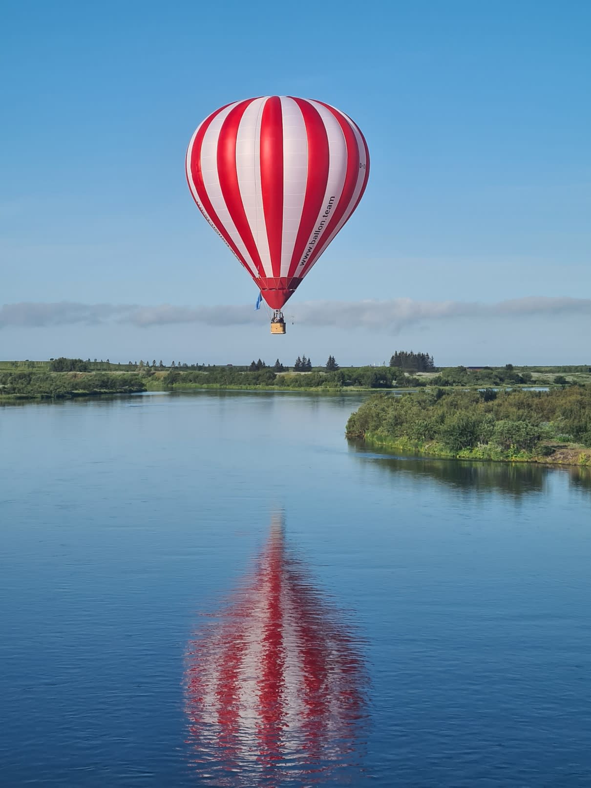 a red and white striped hot air balloon flying over a body of water in South Iceland