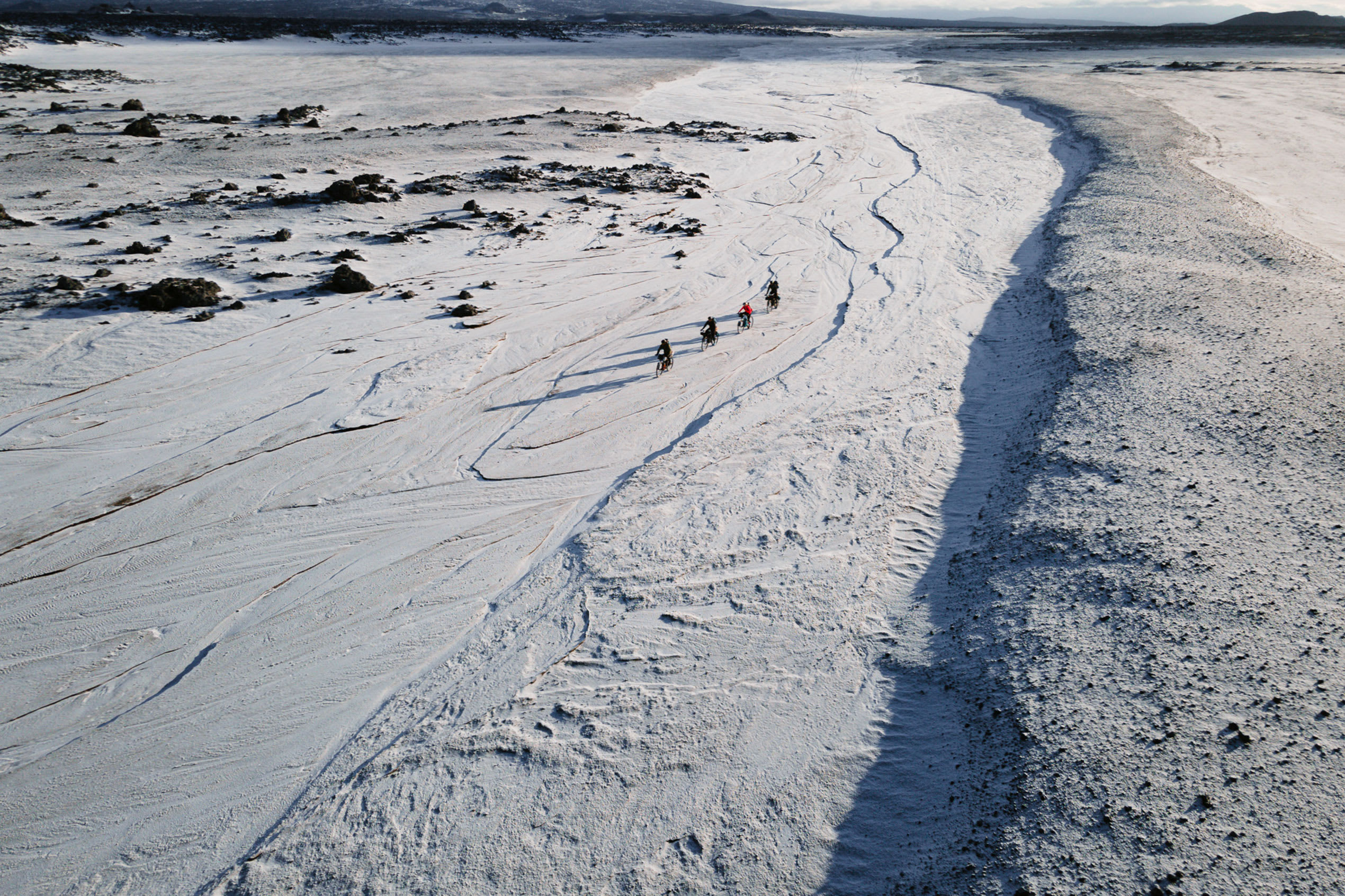 an overhead view of four bikepackers making their way through the snowy Icelandic landscape