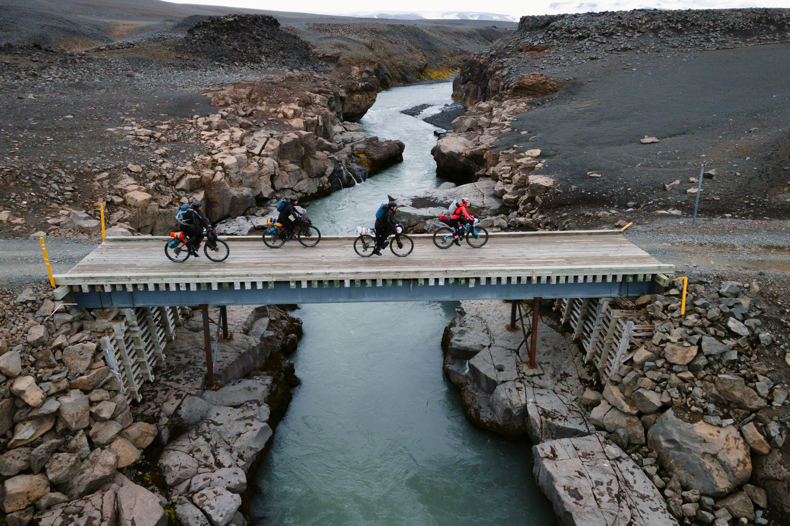 a group of four cyclists bikepacking their way through Iceland, crossing a bride over a river