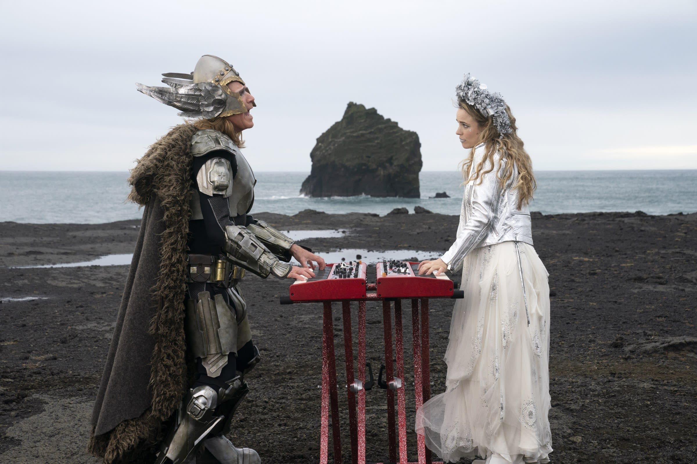 Will Ferrell and Rachel McAdams pictured playing two keyboards while looking at one another and singing. The scene is set amidst the Icelandic landscape