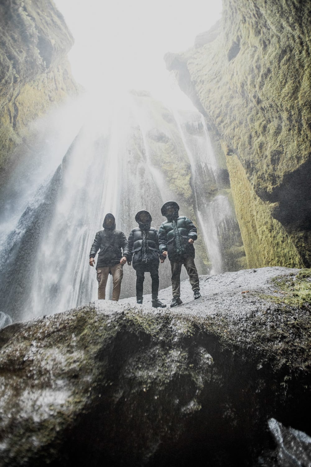 The three members of the Meduza band standing on the rock in front of Gljufrabui waterfall in the South of Iceland looking like they are getting soaked by the waterfall
