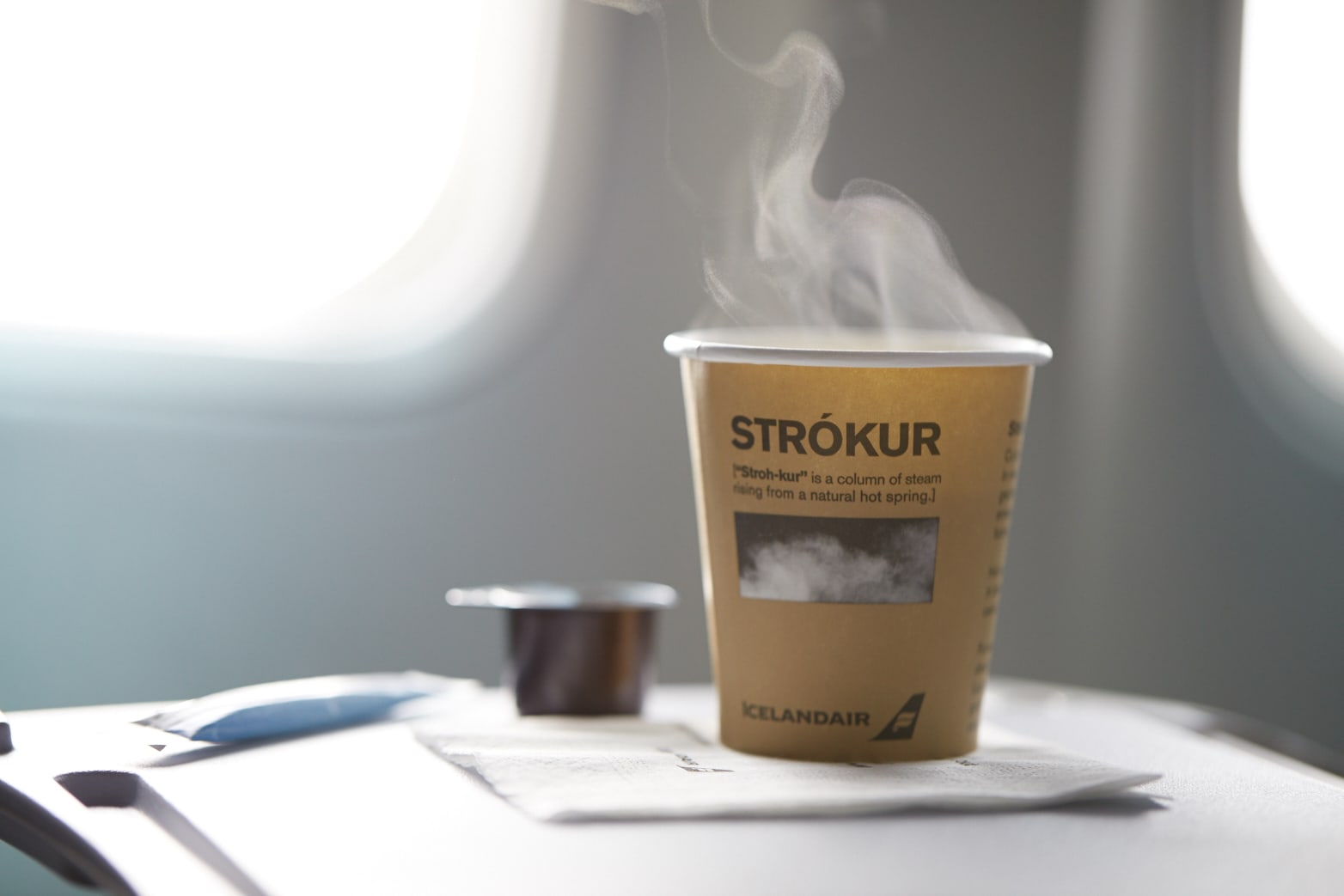 a brown paper cup with a steaming hot drink within it and text printed upon it that reads 'Strokur'