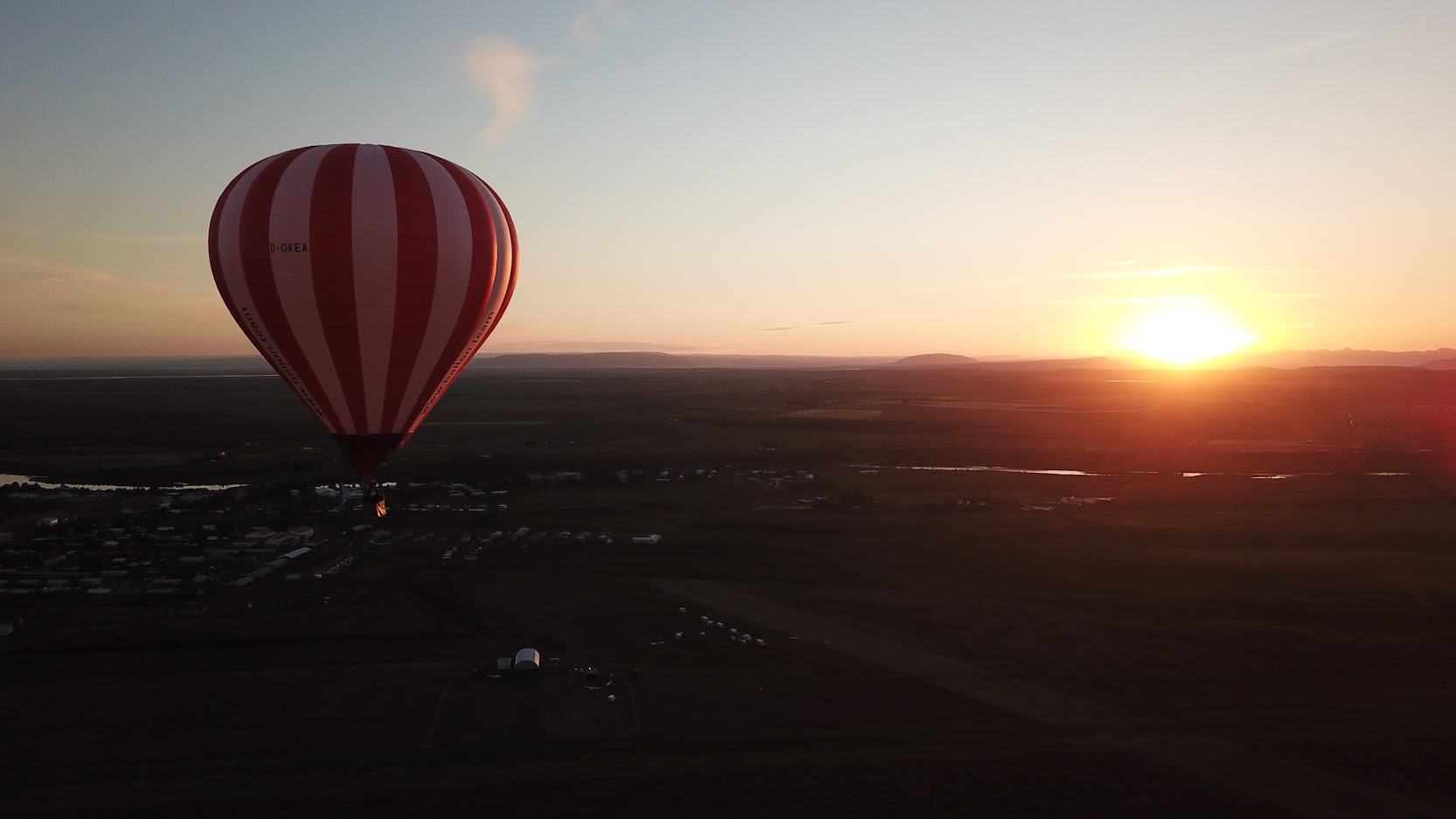 a red and white hot air balloon pictured flying over the South Iceland landscape at golden hour