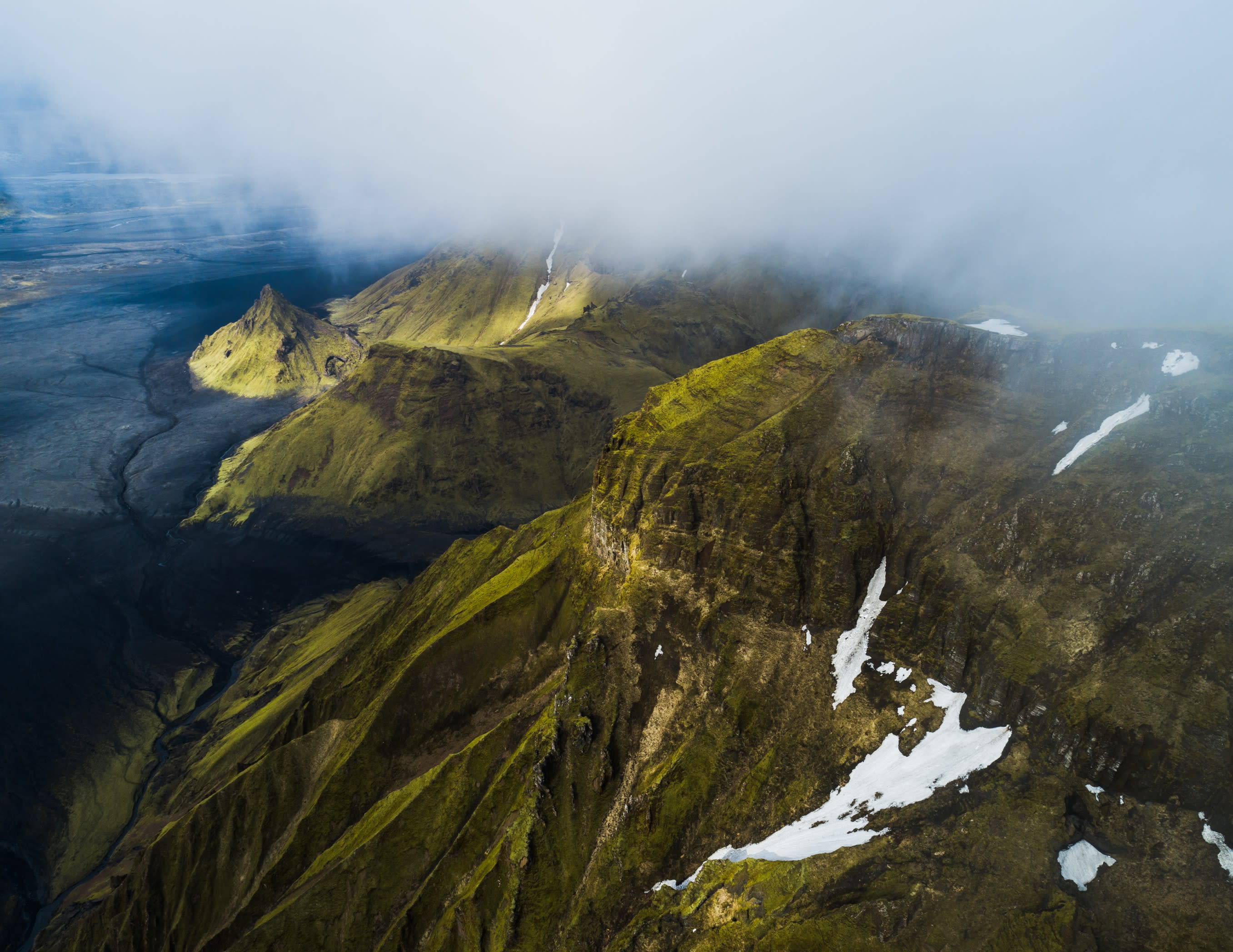 an aerial view of Iceland's diverse landscape: bright green mountaineous regions and black sand plains