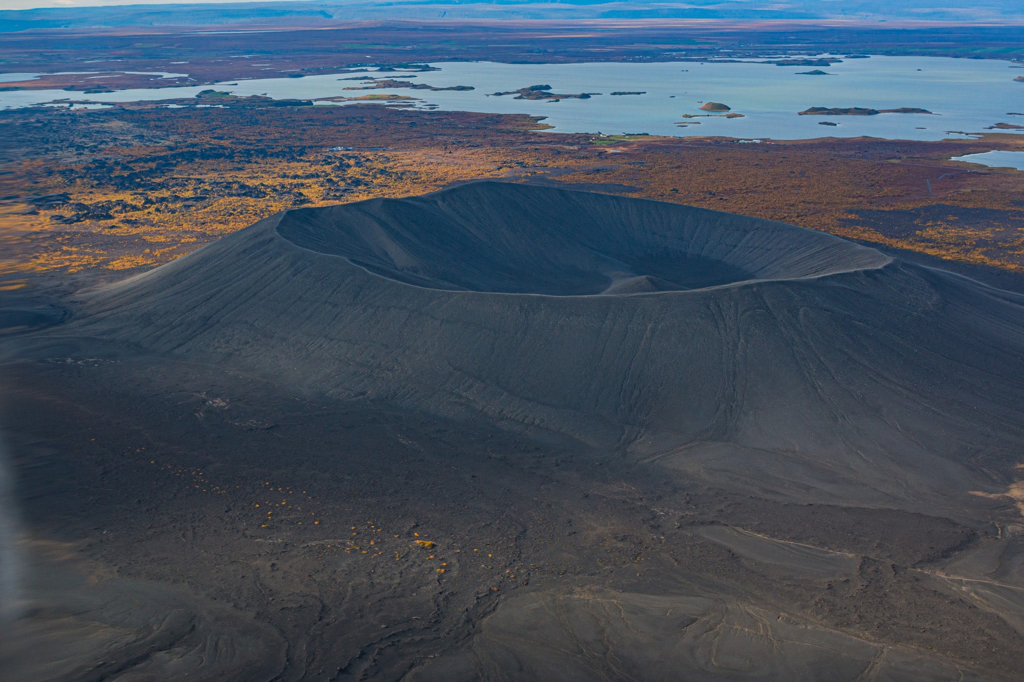 One of Myvatn's large craters pictured from above with views behind of the blue waters and volcanic landscape