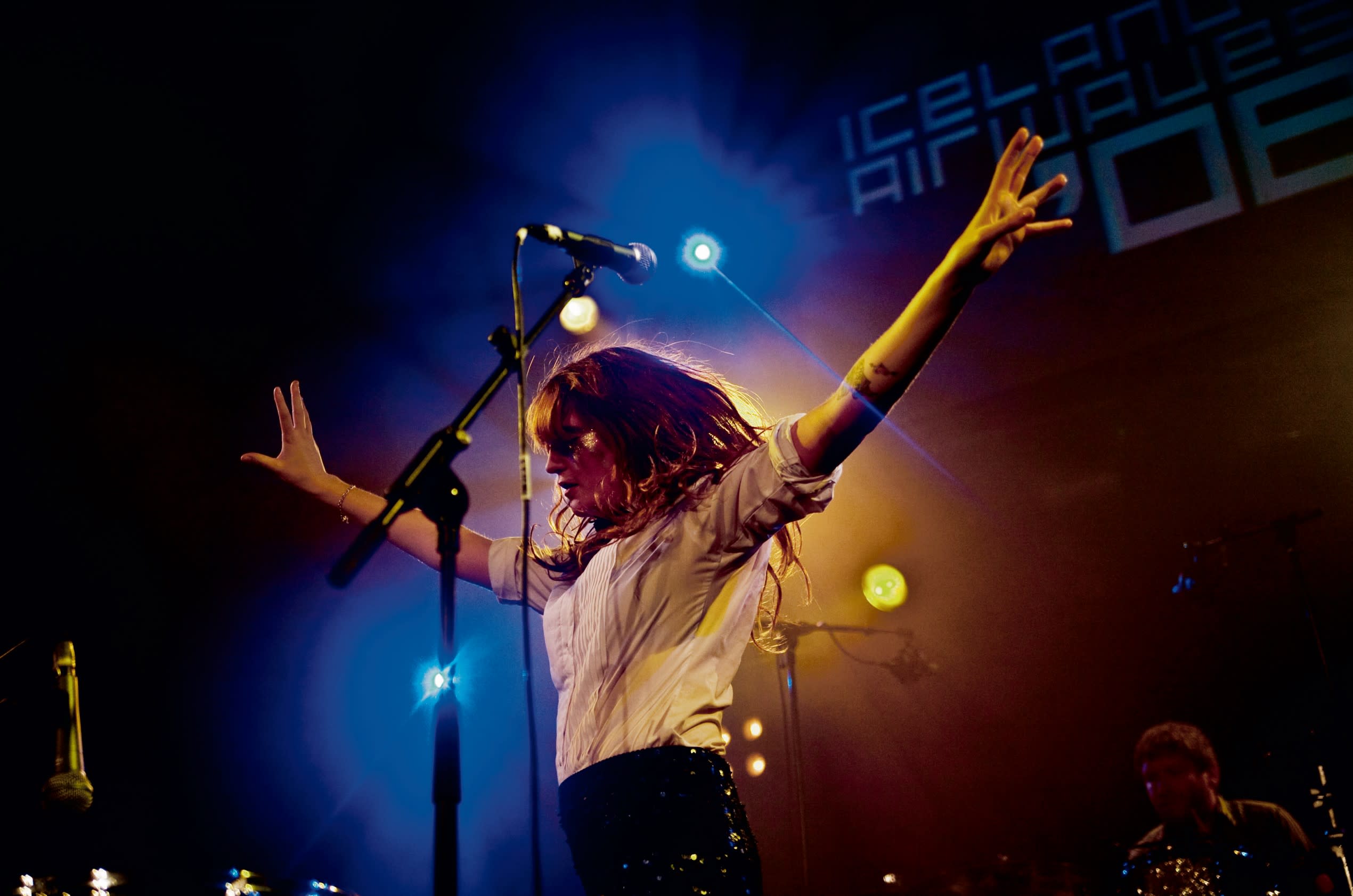 Florence and the Machine performing on-stage with her arms spread wide in dance