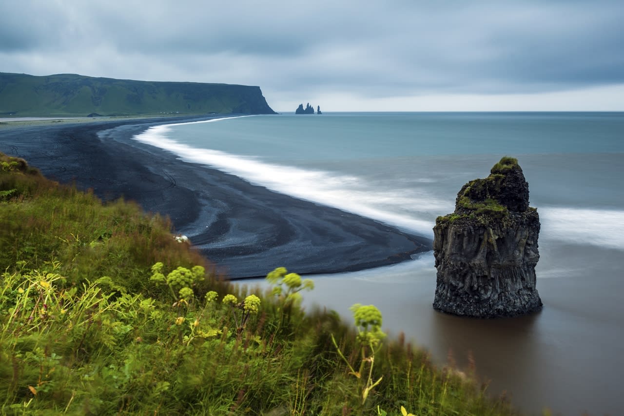 Reynisfjara black sand beach viewed from a hilltop, with the view looking out on to the sea stacks and basalt black columns