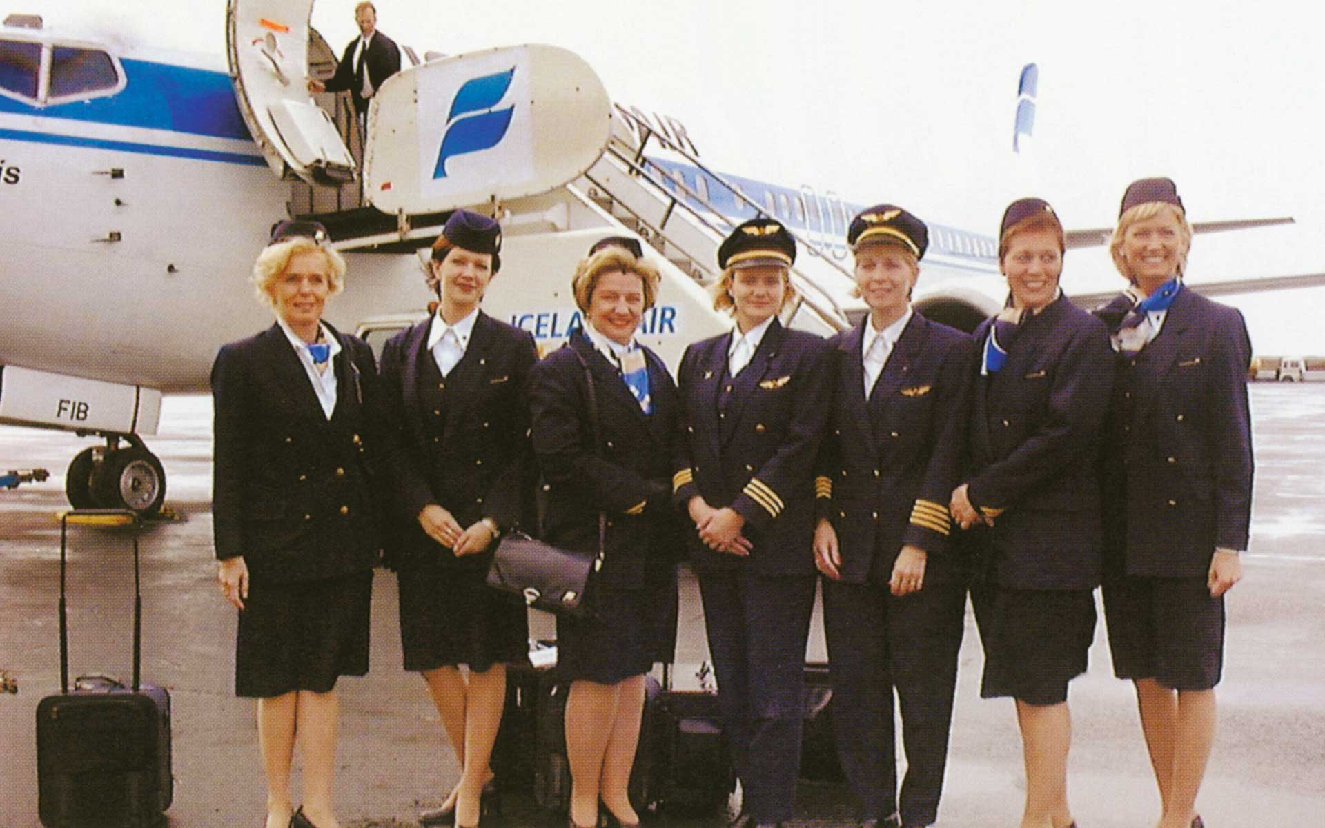 a group of female Icelandair staff wearing full uniform standing in front of an Icelandair airplane