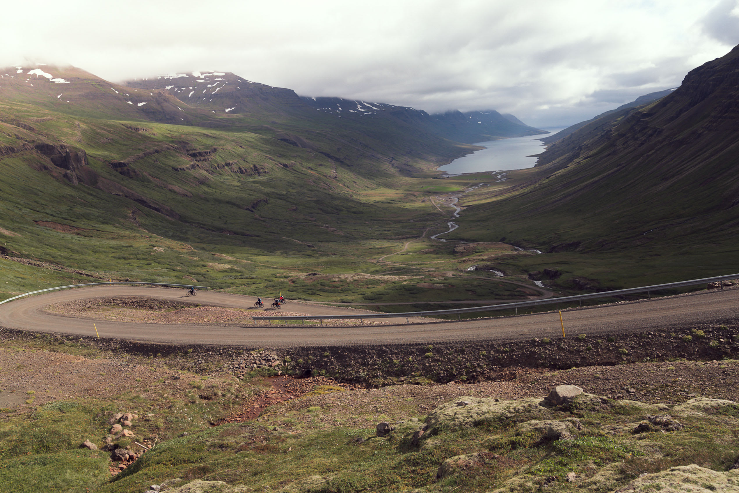 a view of a road weaving down into a fjord in Iceland, with water visible in the far distance