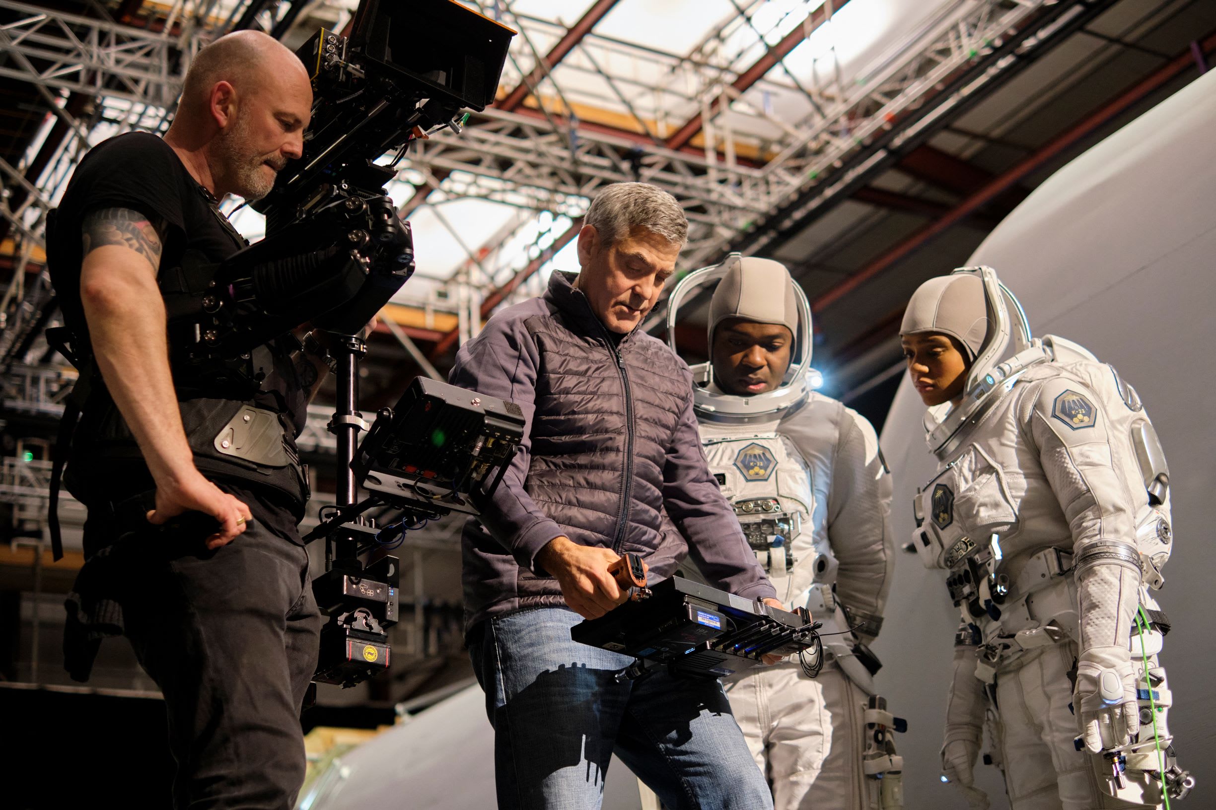 George Clooney pictured looking at an electronic device while standing next to two people dressed in astronaut costumes and another dressed all in black