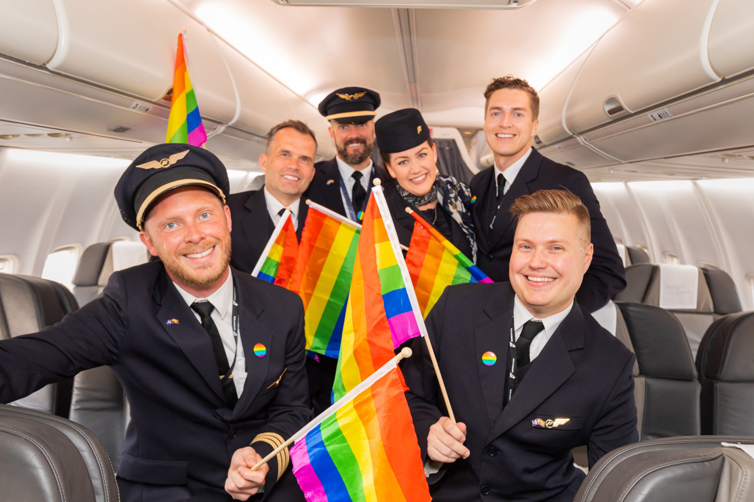 A group of Icelandair pilots and cabin crew inside the aircraft holding rainbow Pride flags