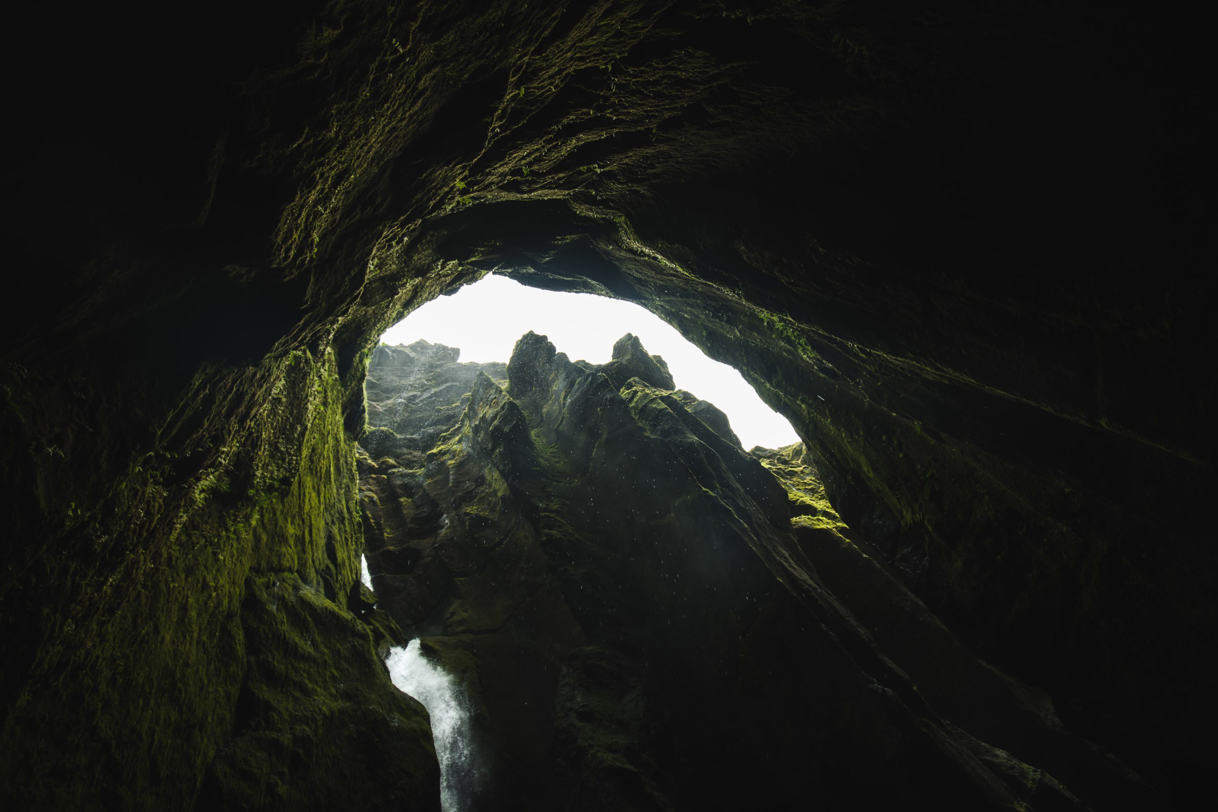 A view from within a cave-like structure with a small body of water in the foreground, looking out towards the light