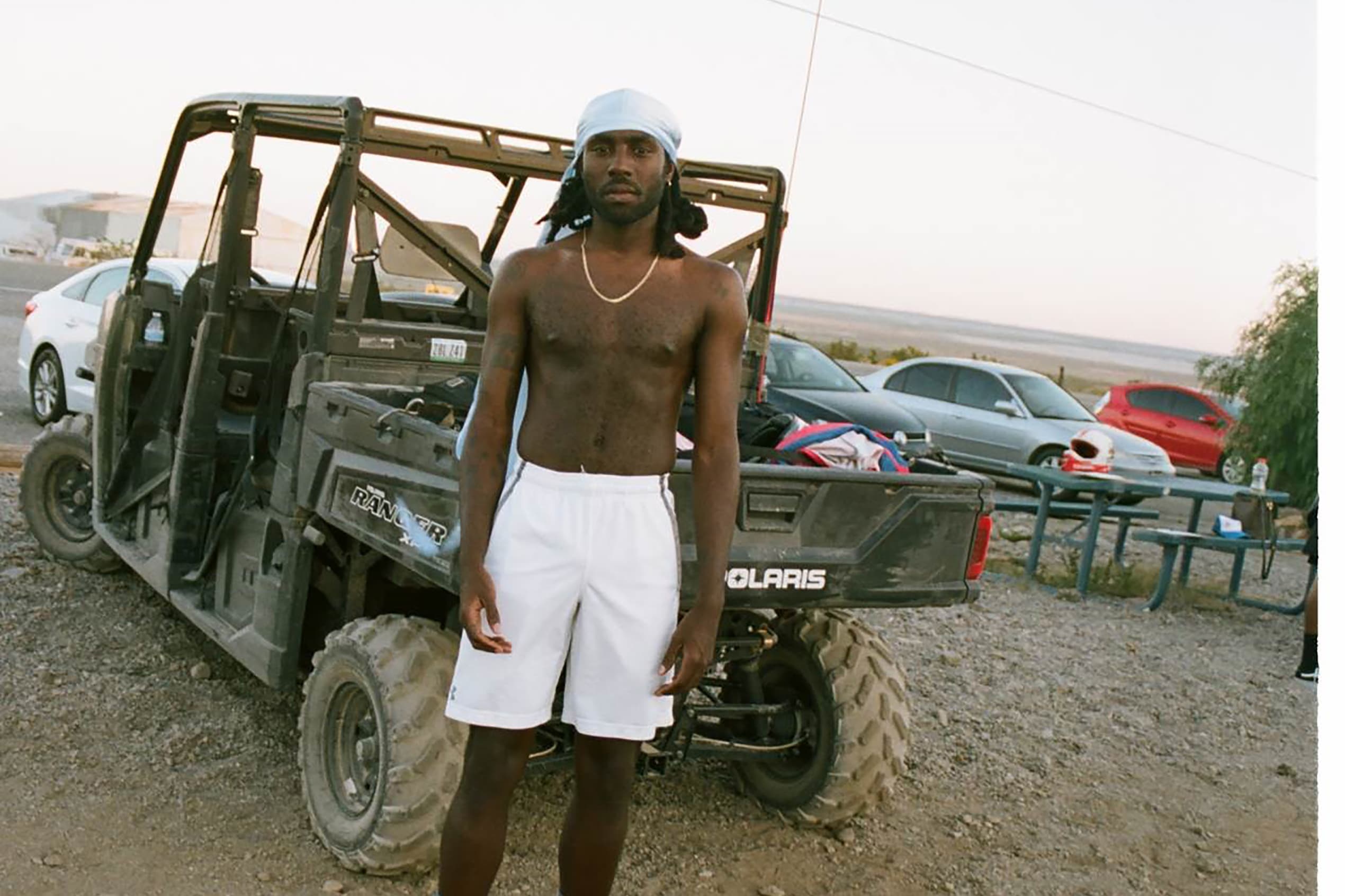 Blood Orange pictured in shorts, standing in front of a black jeep