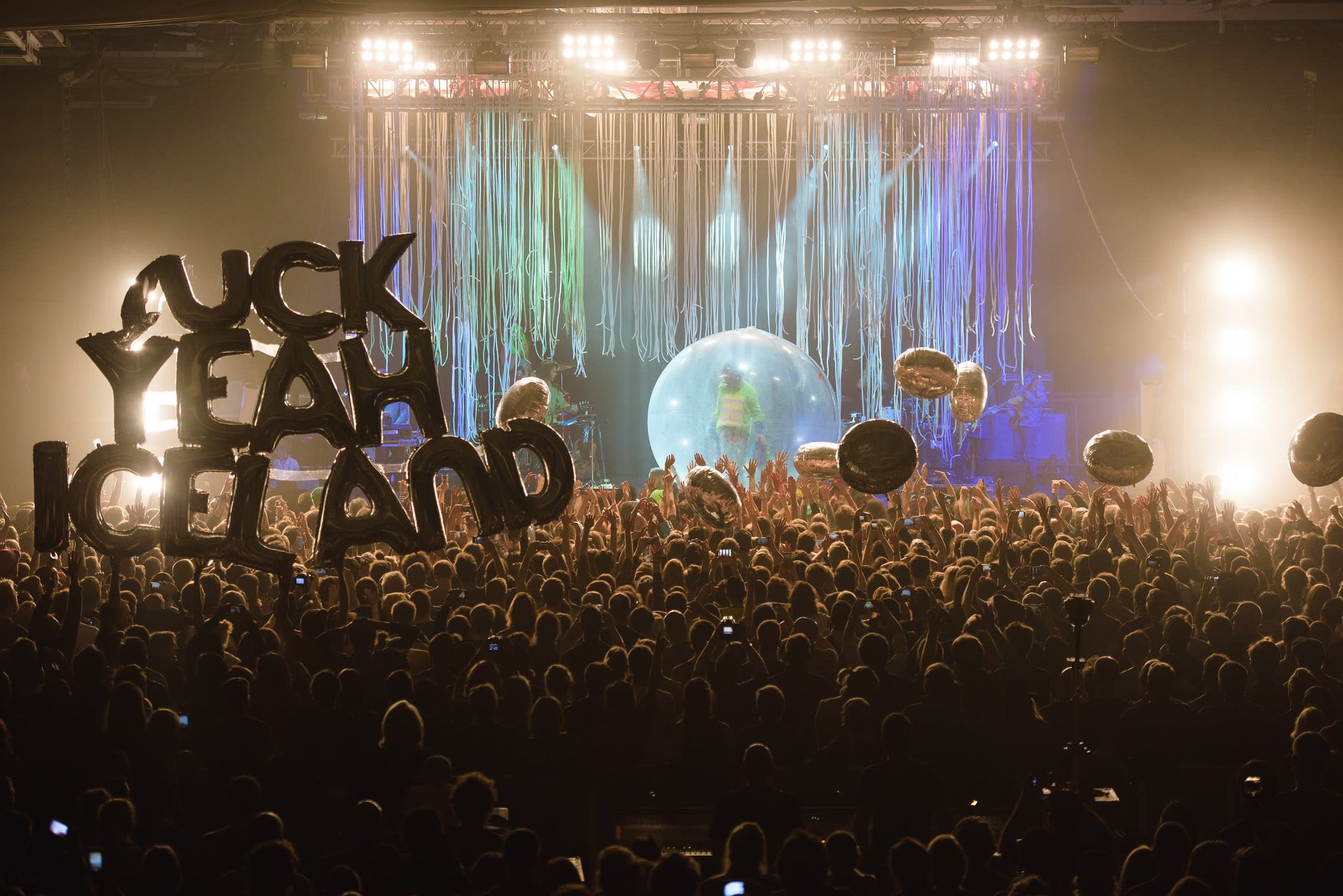 A packed audience watches The Flaming Lips perform onstage at Iceland Airwaves in 2014. An audience member holds a balloon which reads 'F*ck yeah Iceland'