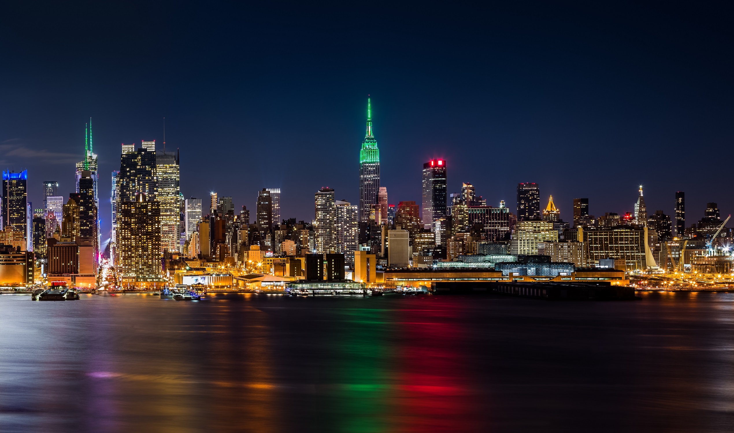 The New York city skyline viewed from the water at night, with the city lights reflecting in the water