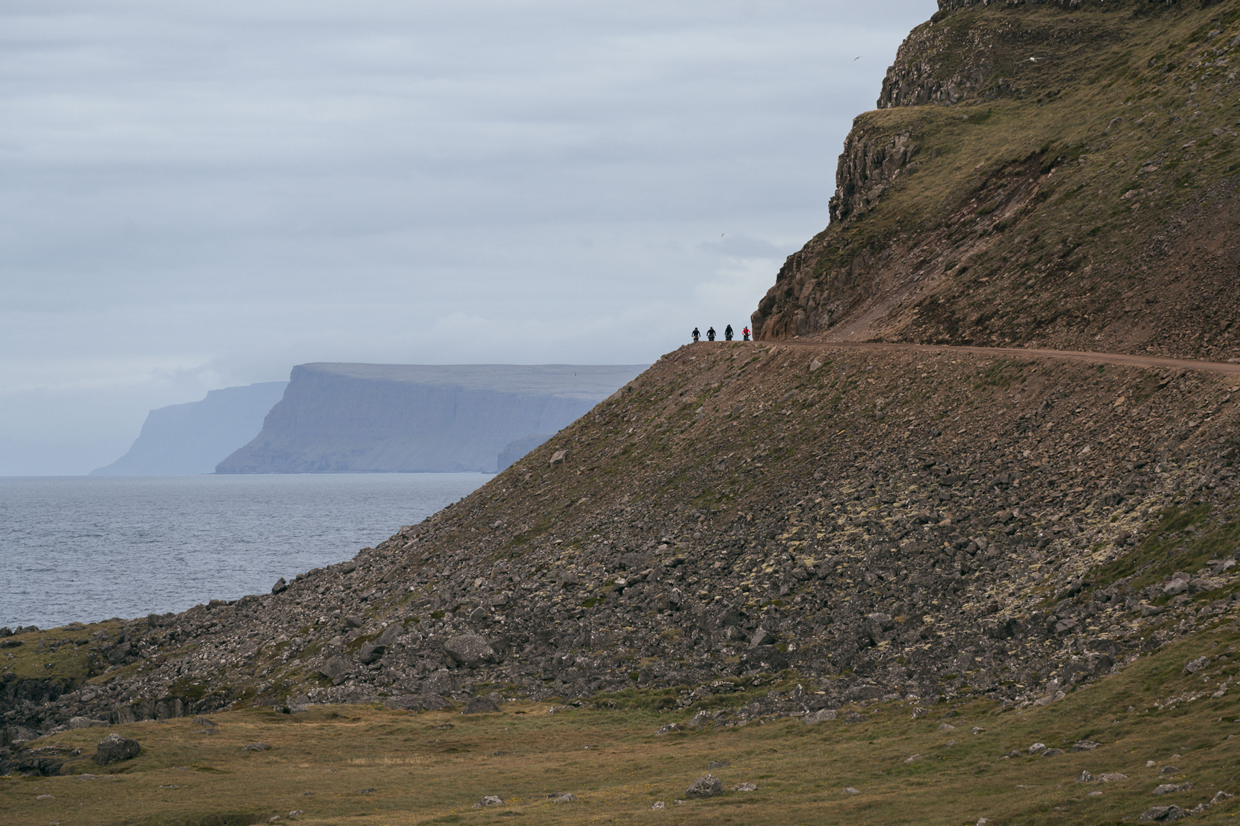 four cyclists pictured in the distance riding over a mountain on a dirt track