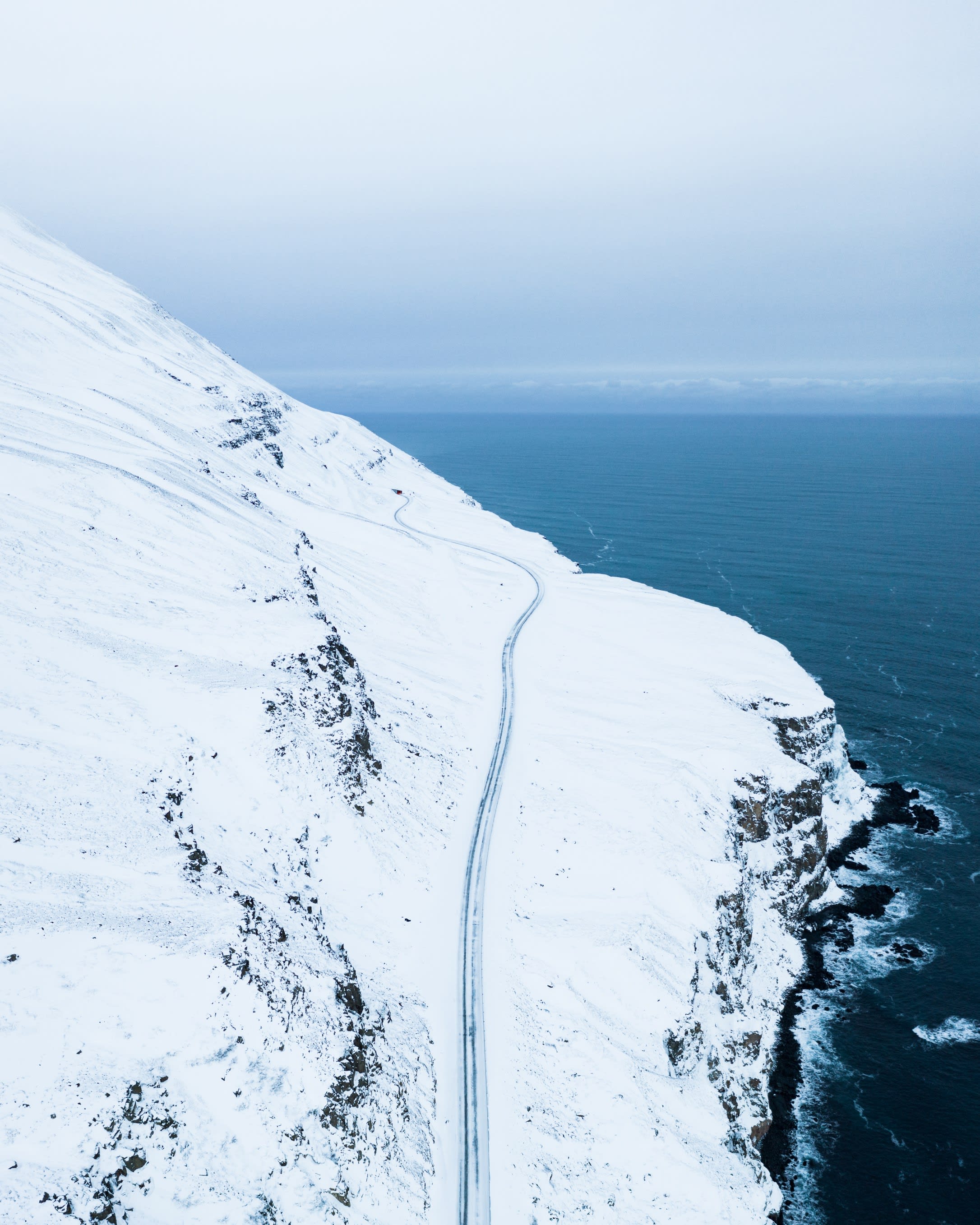 an aerial view of a fjord in Iceland with a road hugging the side of the mountain