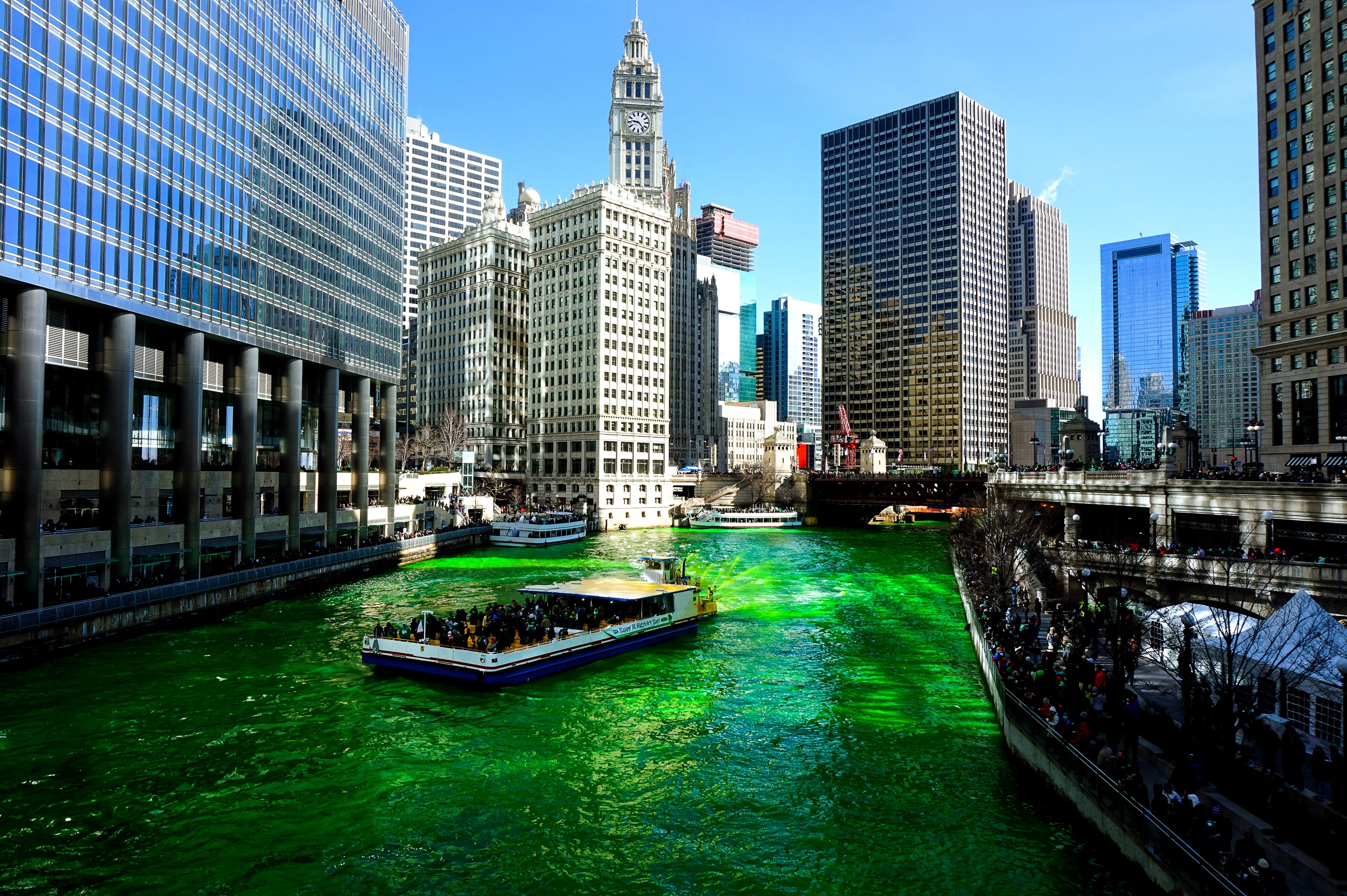 Boston city skyscrapers pictured with boat riding on a body of green water in the foreground