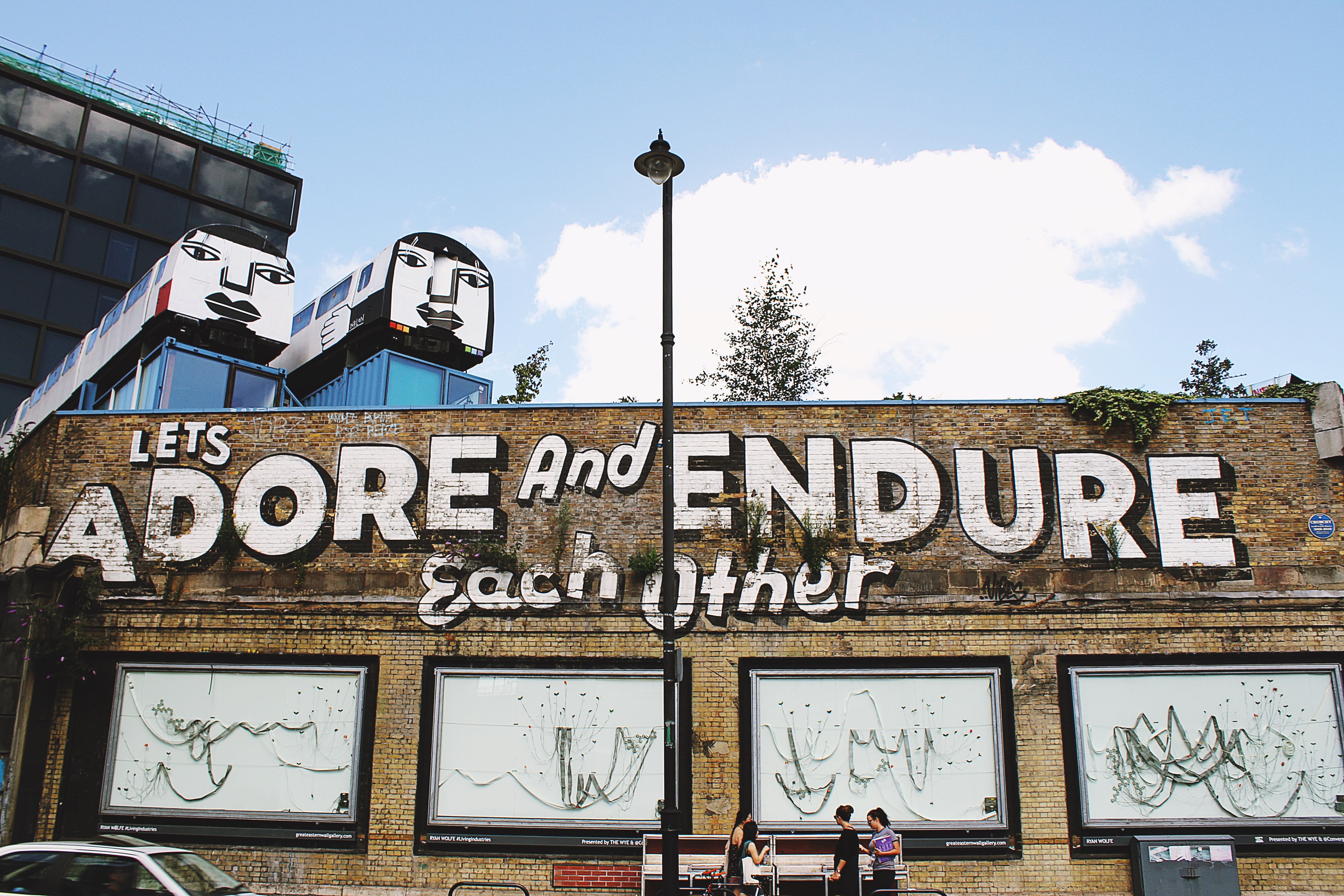 Street art in Shoreditch, painted on a brown brick wall, which reads 'Let's adore and endure each other'