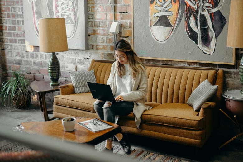 Woman with glasses sitting on a couch working on a laptop